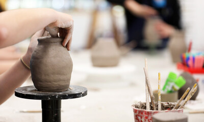 Student's hands working with raw green wet clay in the visual art school classroom. Ceramic class...