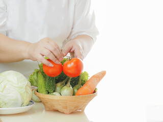 The hands of women aged 50-60 are putting vegetables in a wicker basket on the table , the benefit of fresh vegetables are good for the health of the elderly.