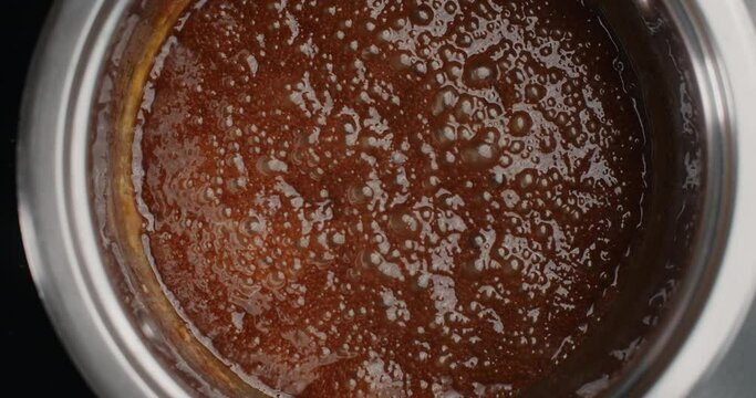 Tabletop slow motion video: Melted sugar is boiling in the metal bowl on the hot stove , making of hot salty caramel, cooking filling for cake, making desserts and candies, 4k 60fps Prores HQ 10 bit