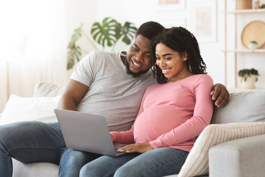 Pregnant couple having fun at home, using laptop together