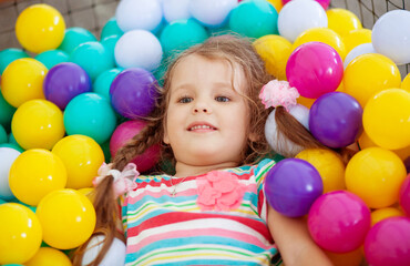 Little cute girl plays in bright colored plastic balls, a child's leisure.
