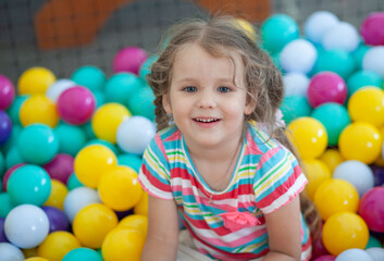 Little cute girl plays in bright colored plastic balls, a child's leisure.
