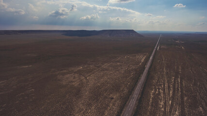Aerial photo from flying drone of a beautiful nature landscape with asphalt road in Texas district. View on a way in countryside and silhouette of mountains against cloudy sky with sun rays