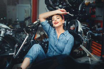 Naklejka na ściany i meble beautiful girl repairs a motorcycle in a workshop, pin-up style, service and sale
