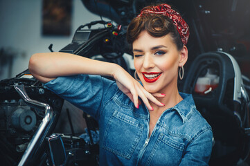 Naklejka na ściany i meble beautiful girl posing repairs a motorcycle in a workshop, pin-up style, service and sale