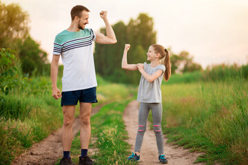 Full length portrait of handsome father and his cute little daughter showing their muscles, looking...