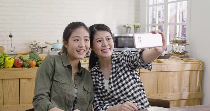 group of asian chinese female friends in kitchen taking selfie on mobile phone. happy ladies make self photo on smartphone in modern cooking place at home. girl roommates having fun in leisure time