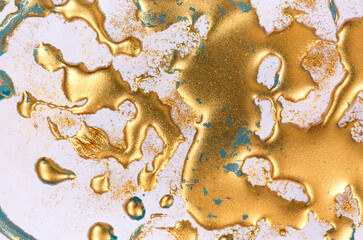 Golden ink drops on white paper background.