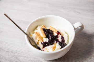 Vanilla ice cream with blackberry jam in a white cup on a wooden light background