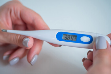 Close up: woman hands holding white digital medical thermometer with high temperature - selective focus. Healthcare, measurement, disease, infection, coronavirus concept