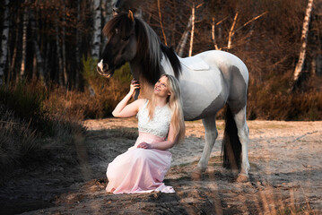 Reiterin kniet vor ihrem Pony an einem See mit einer Spiegelung und schaut zu ihm auf