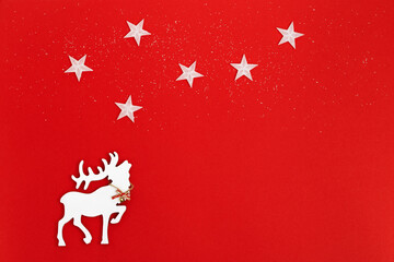 Fototapeta na wymiar Christmas greeting card with handmade white deer in fir tree forest on red background. Star on skyю. Winter Holiday concept.