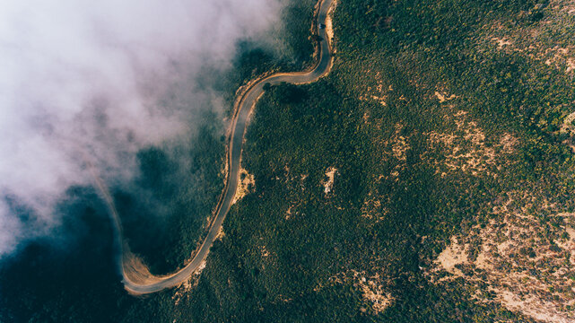 Aerial scenery view of road pass in rocky mountains covered with fog. Bird's eye view through clouds of serpentine asphalt road twists in mountainous terrain on steep slopes - Powered by Adobe