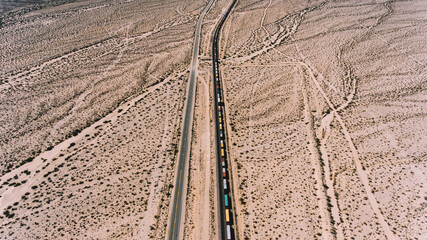 Aerial view of train containers shipping goods in wild environment, locomotive freight on railroad transporting cargo through desert lands in Arizona. Logistic and delivery shipping goods everywhere