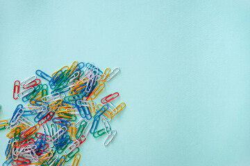 Multi-colored paper clips arranged randomly in the lower left corner of the photo. A pile of objects of white, yellow, green, red and blue colour. Horizontal photo. Flat lay composition on a light
