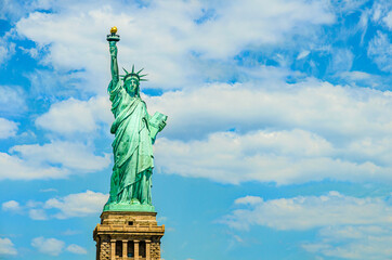 Obraz premium The Statue of Liberty designed by Alexandre Gustave Eiffel on a blue sky with white clouds background with 4th of July writing visible on Liberty Island in New York, USA