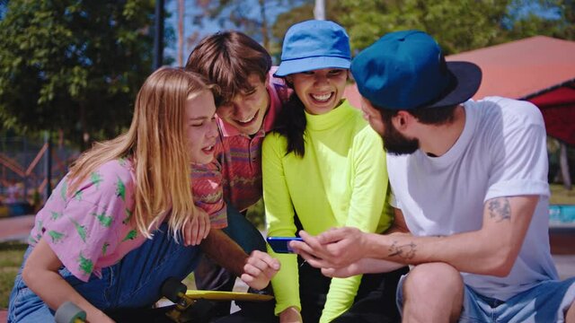 Very happy and excited group of hipster friends in a urban skate park have a socializing time they looking through the modern smartphone concept of a media lifestyle internet education