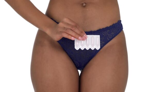 Unrecognizable Latin woman in blue panties and with bare belly holding vaginal suppository. Prescription from gynecologist for women's health. Isolated, on white background