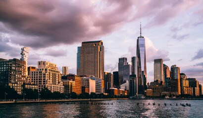 Naklejka premium Panoramic view of Manhattan Island with buildings and Hudson river. Scenery skyline view of contemporary glass skyscrapers of downtown financial district in New York. Dramatic sunset sky over city