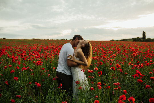 Passionate girl hugging her boyfriend. The guy kisses the girl in the neck. Couple in love. Scarlet poppy field. Casual style. Copy space.