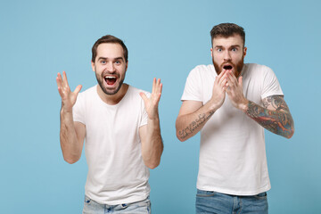 Shocked men guys friends in white t-shirt isolated on pastel blue background. Sport leisure lifestyle concept. Mock up copy space. Cheer up support favorite team, keeping mouth open, spreading hands.