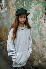 City portrait of handsome girl kid wearing gray blank hoodie or sweatshirt and cap with space for your logo or design. Mockup for print