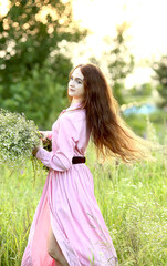 Young beautiful red-haired girl in a pink dress is spinning with a huge bouquet of summer daisies in the garden at sunset. The effect of bokeh, flash, sun rays. Summer. The concept of relaxation