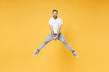 Fototapeta na wymiar Cheerful young bearded man guy in white casual t-shirt posing isolated on yellow wall background studio portrait. People sincere emotions lifestyle concept. Mock up copy space. Jumping spreading legs.