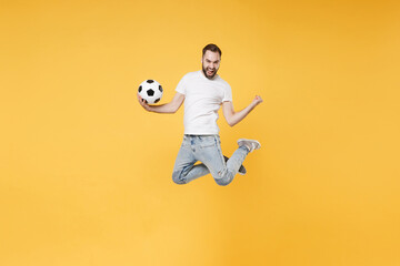 Fototapeta na wymiar Joyful bearded man guy football fan in white t-shirt isolated on yellow background. People sport family leisure concept. Cheer up support favorite team with soccer ball, jumping, doing winner gesture.