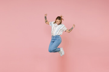 Happy young blonde woman girl in casual striped shirt posing isolated on pastel pink background studio portrait. People emotions lifestyle concept. Mock up copy space. Jumping, doing winner gesture.