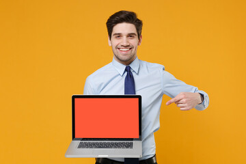 Smiling young business man in classic blue shirt tie isolated on yellow background. Achievement career wealth business concept. Pointing index finger on laptop pc computer with blank empty screen.