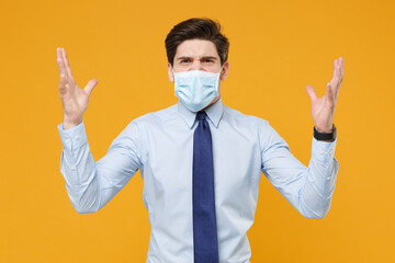 Irritated business man in blue shirt tie sterile face mask isolated on yellow background. Epidemic pandemic rapidly spreading coronavirus 2019-ncov sars covid-19 flu virus concept. Spreading hands.