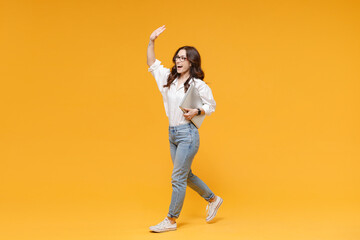 Fototapeta na wymiar Excited young business woman in white shirt glasses isolated on yellow background. Achievement career wealth business concept. Hold laptop pc computer waving and greeting with hand as notices someone.