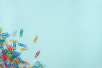 Obraz na płótnie Canvas Multi-colored paper clips arranged randomly in the lower left corner of the photo. A pile of objects of white, yellow, green, red and blue colour. Horizontal photo. Flat lay composition on a light