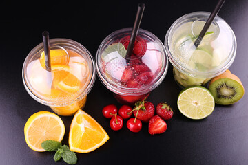 Lemonade to go. Three cups with mint, cherry, strawberry, kiwi, lime, orage, lemon on black background, isolated