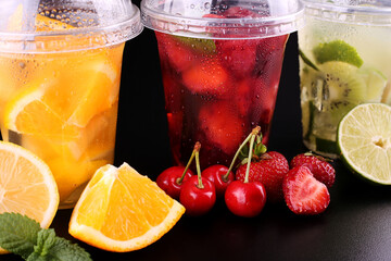 Lemonade to go. Three cups with mint, cherry, strawberry, kiwi, lime, orage, lemon on black background, isolated