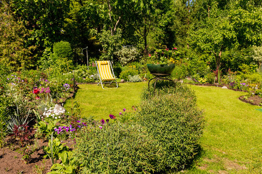 A fragment of a garden plot with various colors and a yellow deck chair on a green lawn.