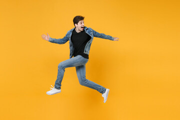 Fototapeta na wymiar Excited young man guy 20s wearing casual denim clothes posing isolated on yellow background studio portrait. People emotions lifestyle concept. Mock up copy space. Jumping like running, looking aside.