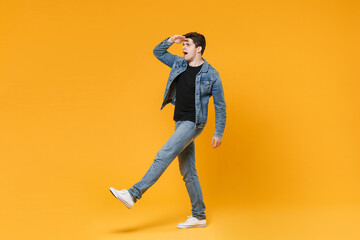 Shocked young man guy wearing casual denim clothes posing isolated on yellow background studio portrait. People lifestyle concept. Mock up copy space. Hold hand at forehead looking far away distance.