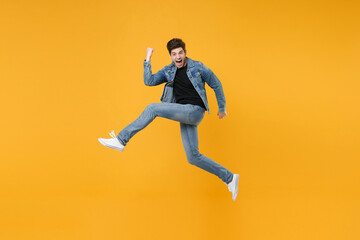 Fototapeta na wymiar Screaming young man guy wearing casual denim clothes posing isolated on yellow background studio portrait. People lifestyle concept. Mock up copy space. Jumping, spreading legs doing winner gesture.