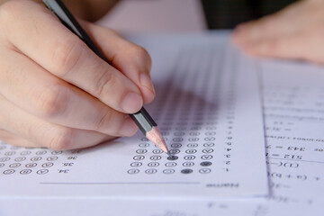 Students hand holding pencil writing selected choice on answer sheets and Mathematics question sheets. students testing doing examination. school exam.