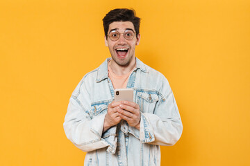 Photo of delighted young man screaming and using mobile phone