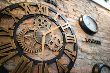 An antique design clock with roman number that installed on the brick wall, interior decorate in the loft style hostel. Close up and selective focus photo.