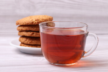 homemade cookies and a glass cup of black tea on the rustic white wooden background. close up