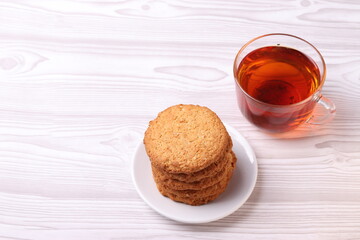 homemade cookies and a glass cup of black tea on the rustic white wooden background. close up