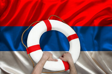 male hands hold on a white life buoy against the background of the silk national flag of the country of Serbia, the concept of medical insurance, tourism, disaster, humanitarian aid