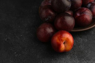 Blue and red pears in ceramic plate on dark stone textured table. Red plum in the foreground. Selective focus. Natural fruit background. Copy space.