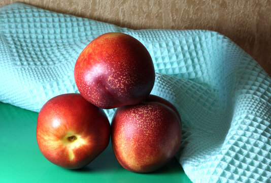 Three nectarines. Whole fruit. Peaches on a green background with a towel.