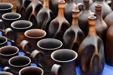 Fototapeta na wymiar Clay jugs and mugs stand in rows on a dark