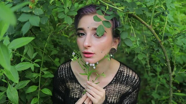 stylish girl with bright short hair with lenses in her eyes and a piercing in a dark dress on a background of nature